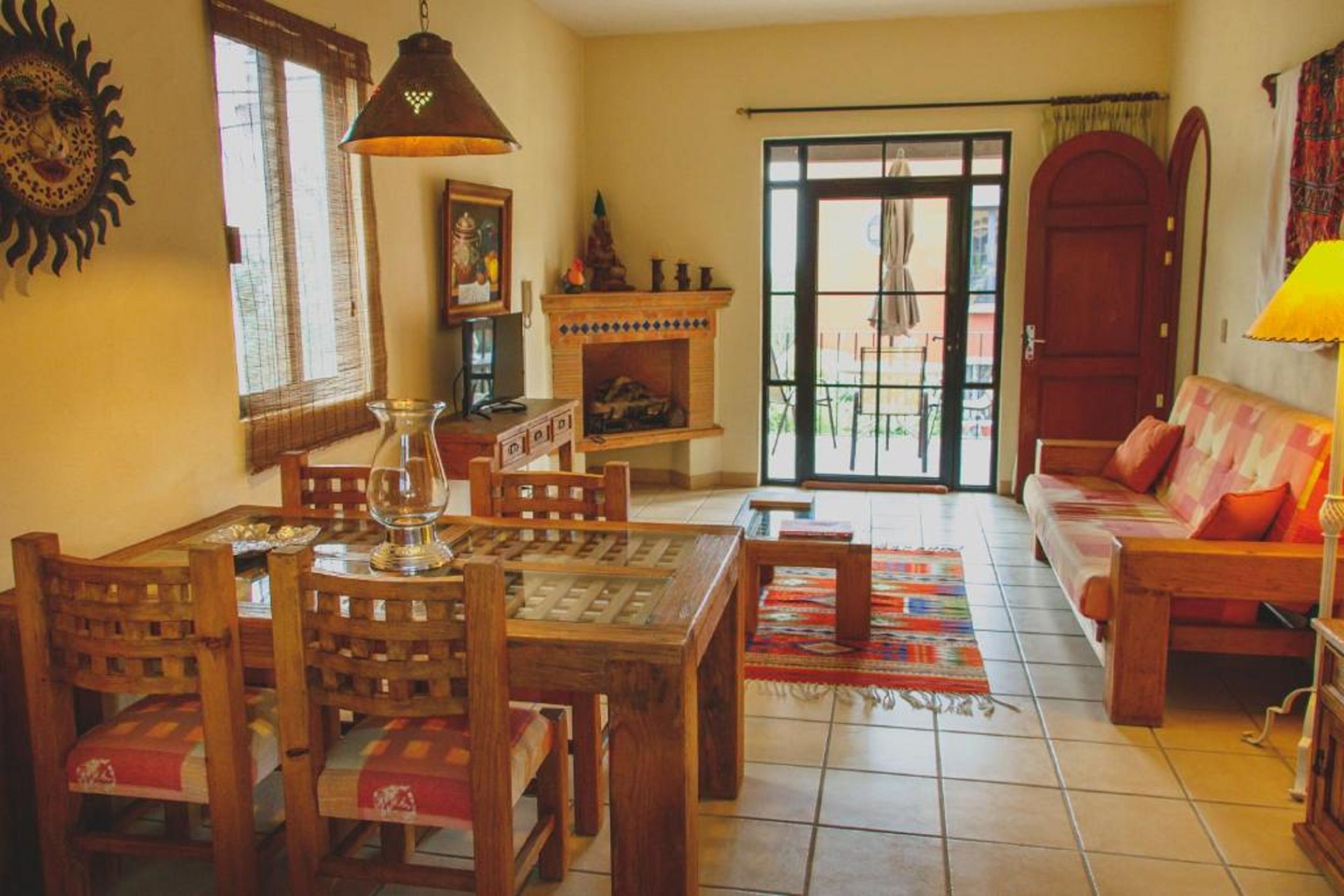 A cozy living room with a wooden dining table, chairs, a sofa, a fireplace, and a large window with a view.
