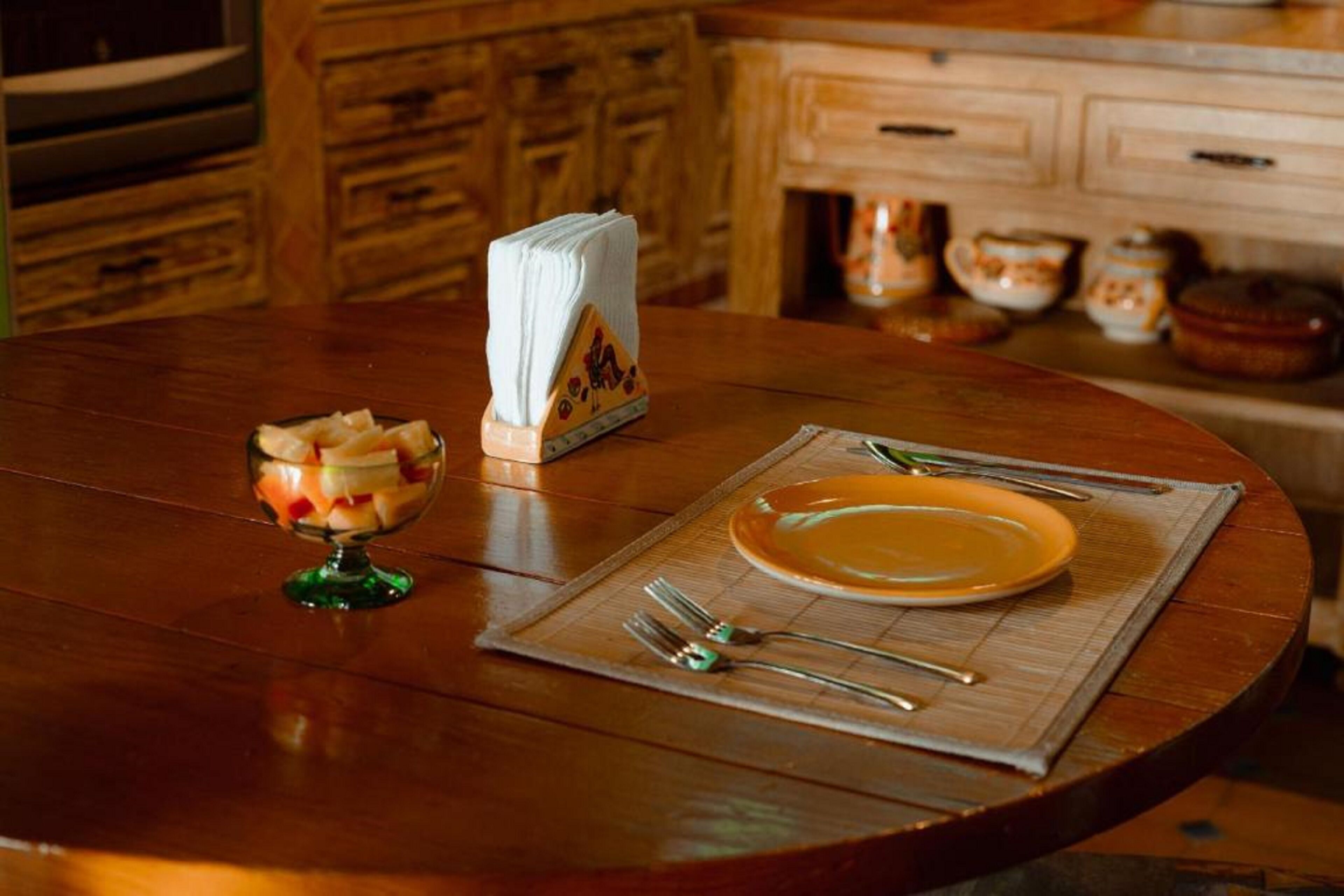 A wooden dining table with a placemat, a plate, cutlery, and a glass of fruit.