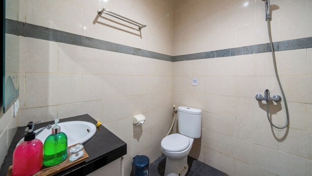 A small bathroom with a toilet, sink, and shower. There are toiletries on the sink counter. - The Kutaya (Kuta)