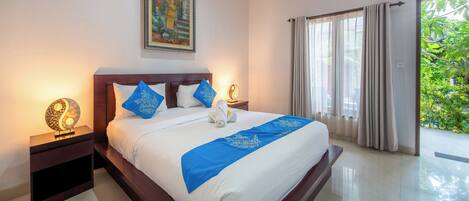 Habitación de hotel con una cama grande, una mesita de noche con lámpara, un cuadro en la pared y vistas a zonas verdes por la ventana.