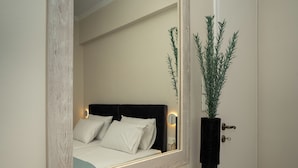 A bedroom with a bed, a bedside table, a mirror, and a potted plant.