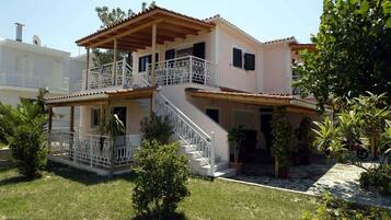 A two-story house with a balcony, a staircase, and a garden with potted plants.