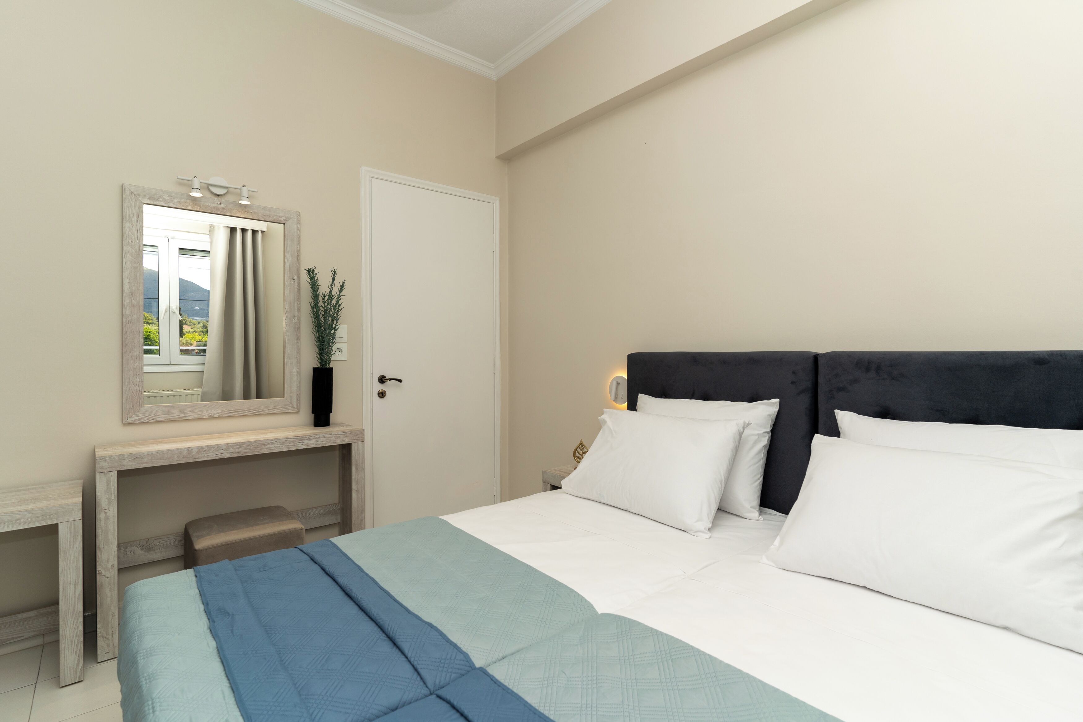 A bedroom with a bed, a bedside table, a mirror, and a door.