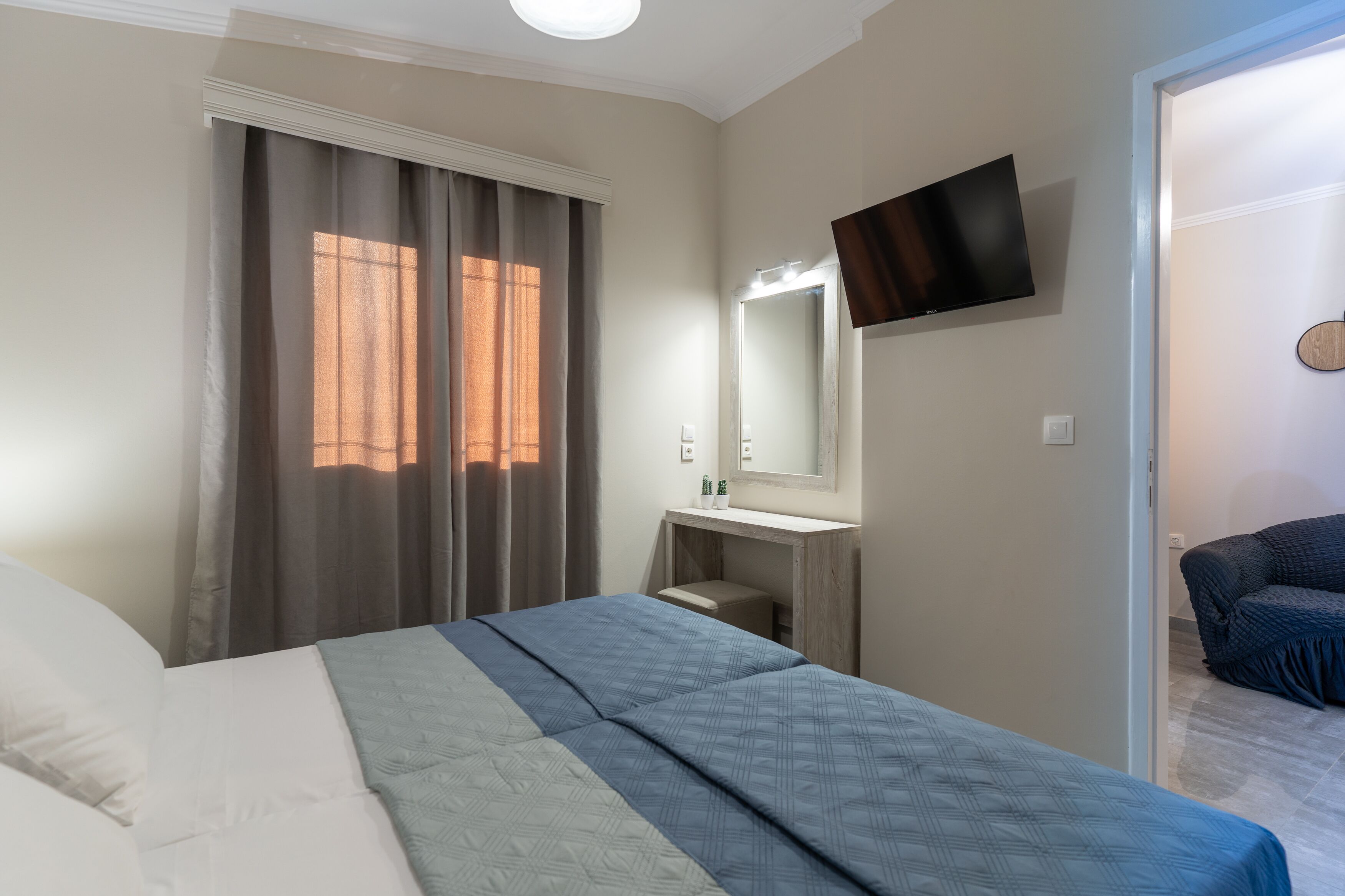 Un dormitori amb un llit, una taula de nit, un mirall, un televisor fixat a la paret i una porta que dona a una altra habitació.