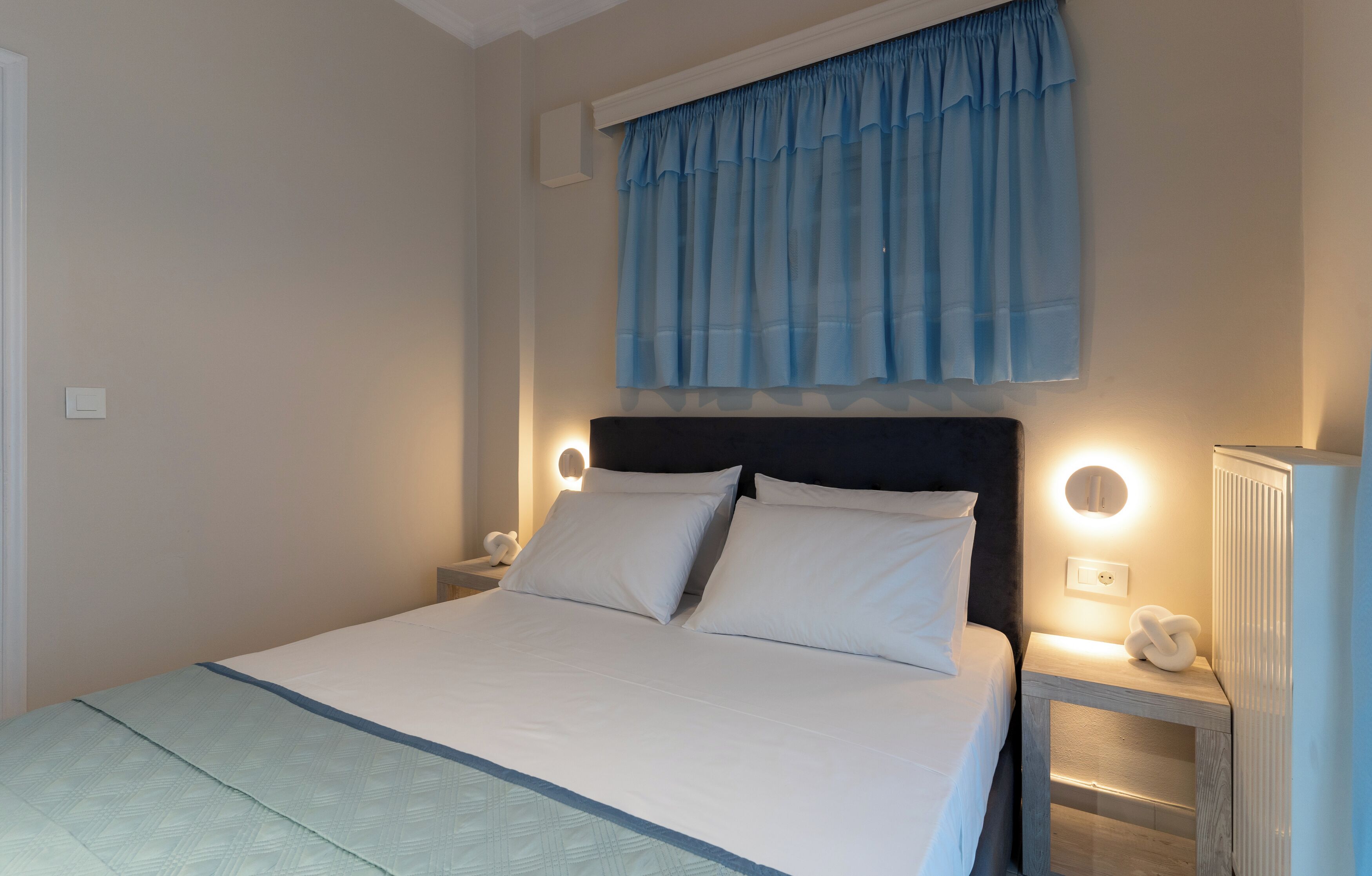 A neatly made bed with white linens, a dark headboard, and two bedside lamps.
