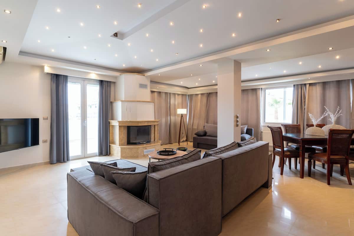 Un salon moderne comprenant un canapé d’angle, une cheminée, une table à manger avec des chaises et un téléviseur à écran plat fixé au mur.