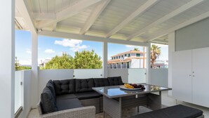 A covered outdoor seating area with a sofa, table, and bench, overlooking a residential neighborhood.