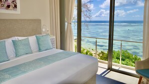 A bedroom with a large bed, a nightstand, and a view of the ocean through a sliding glass door.