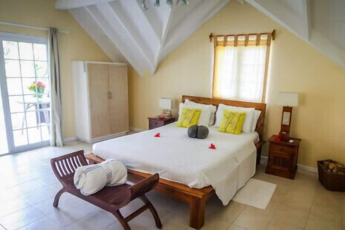 Un dormitorio con cama, una silla, una mesita de noche, una lámpara y un ventanal con cortinas.