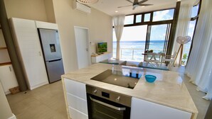 A modern kitchen with a built-in oven, a refrigerator, and a large window overlooking the sea.