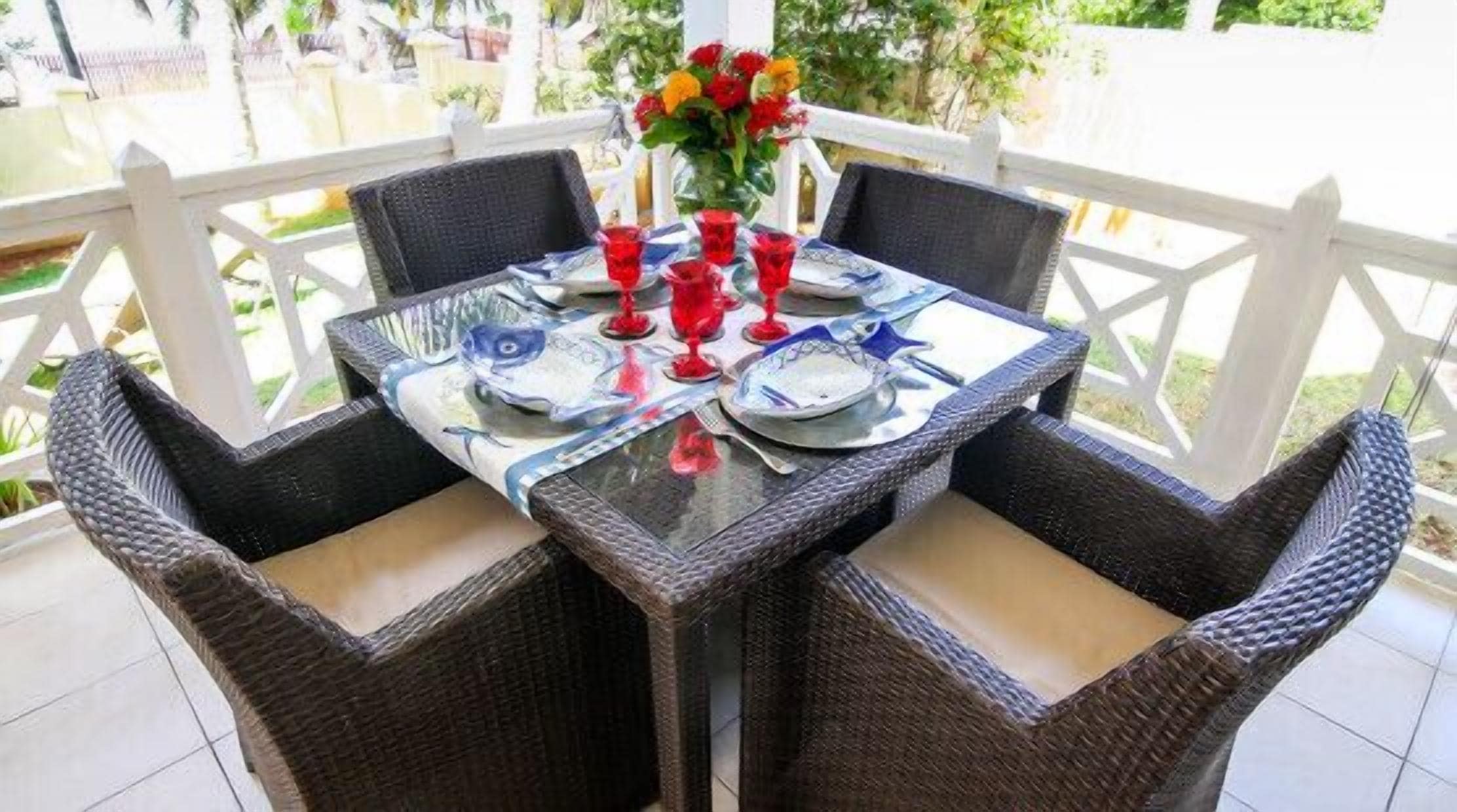 A table set for four with wicker chairs, a glass table, and red glasses.