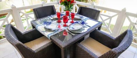 A table set for four with wicker chairs, a glass table, and red glasses.