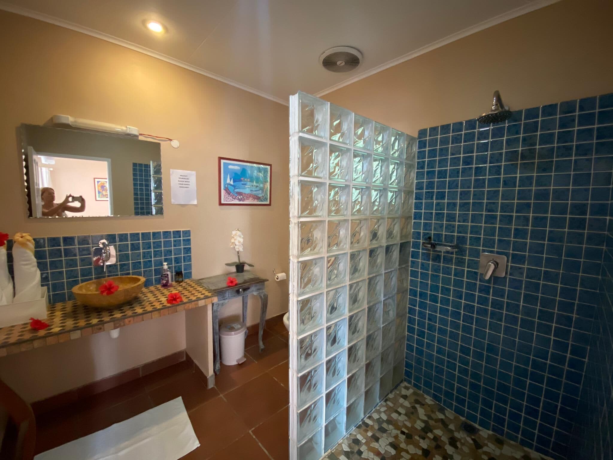 Un baño con ducha de azulejos azules, un lavabo con un recipiente de madera y un espejo encima.