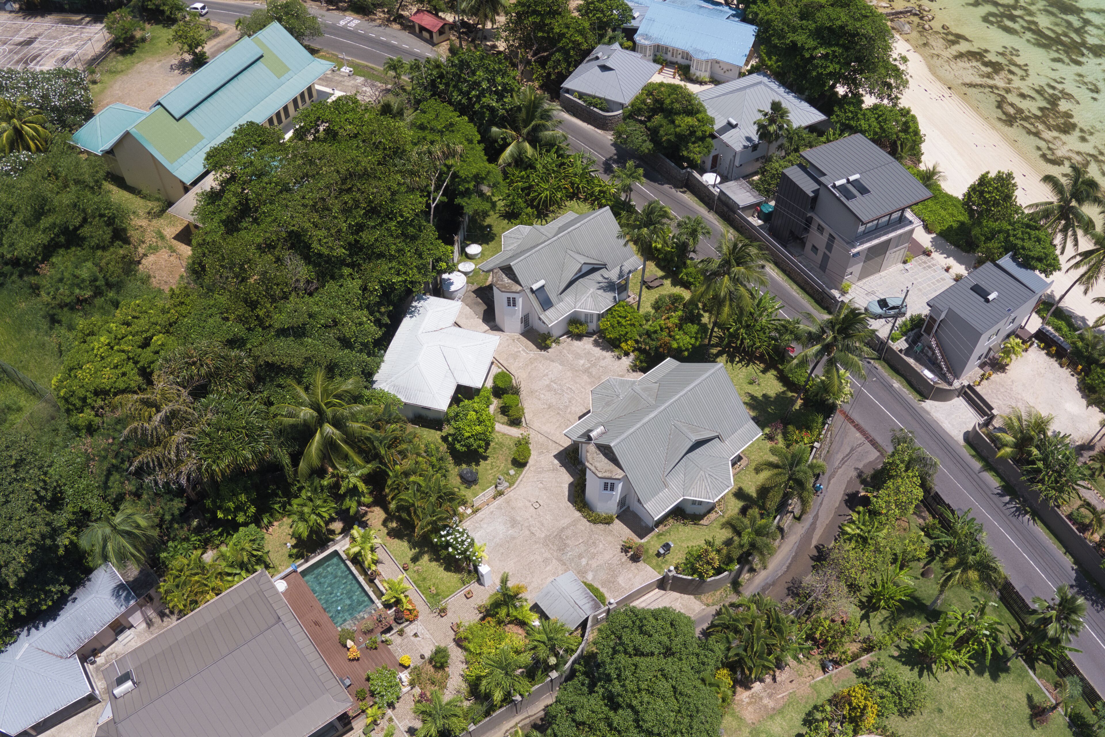 An aerial view of a residential area with houses, a swimming pool, and a beach.