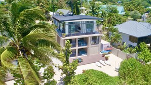 A modern two-story building with a balcony, surrounded by lush greenery and palm trees.