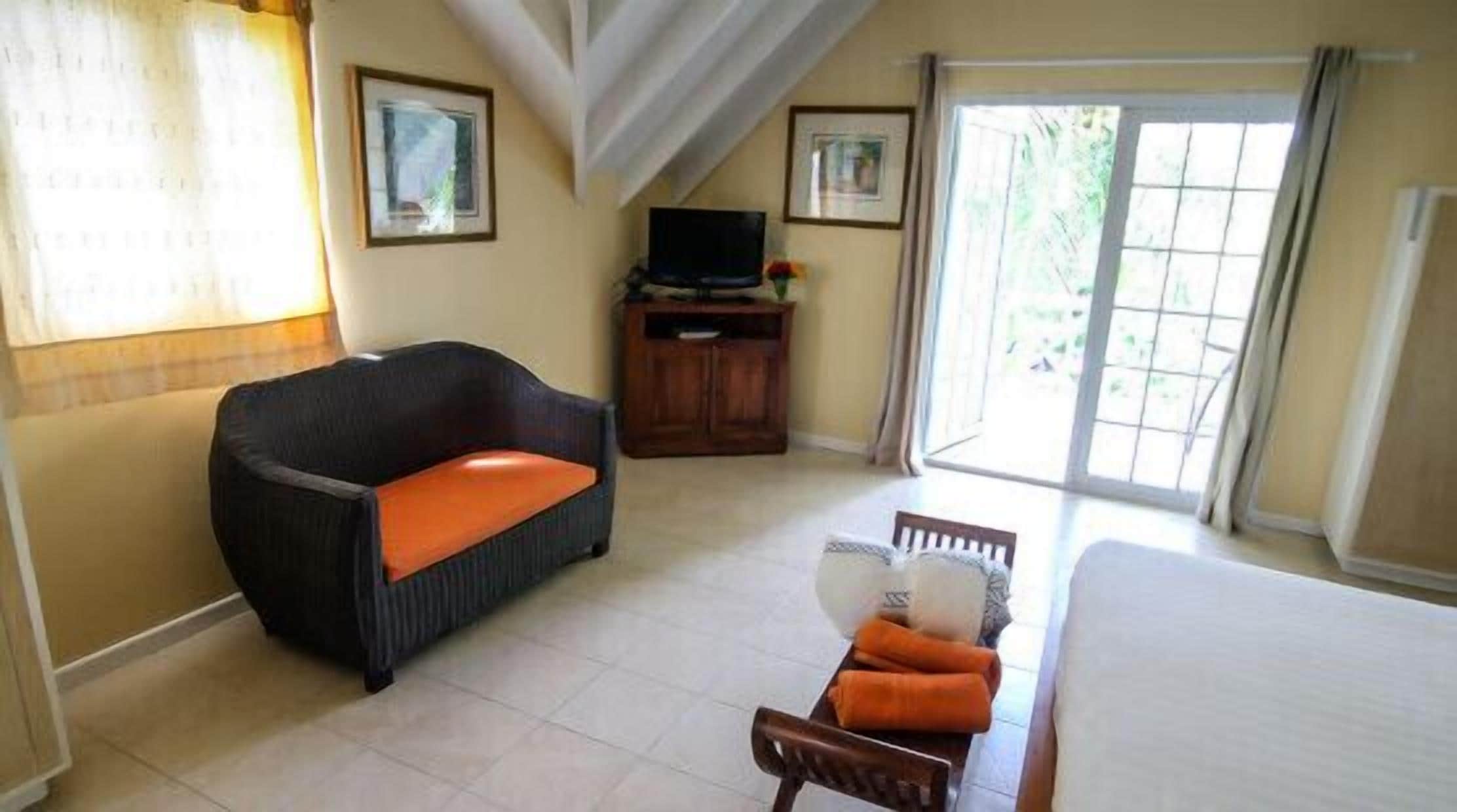 Una habitación de hotel con sofá, televisor, mesa de comedor con sillas y un ventanal grande.