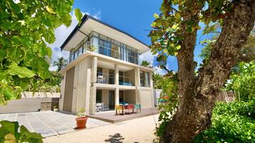 Una casa moderna de dos pisos con un balcón, un patio con mobiliario exterior y un árbol en primer plano.