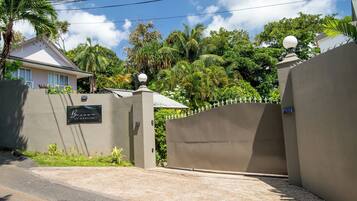 A gated entrance with a sign, a paved driveway, and lush greenery in the background.