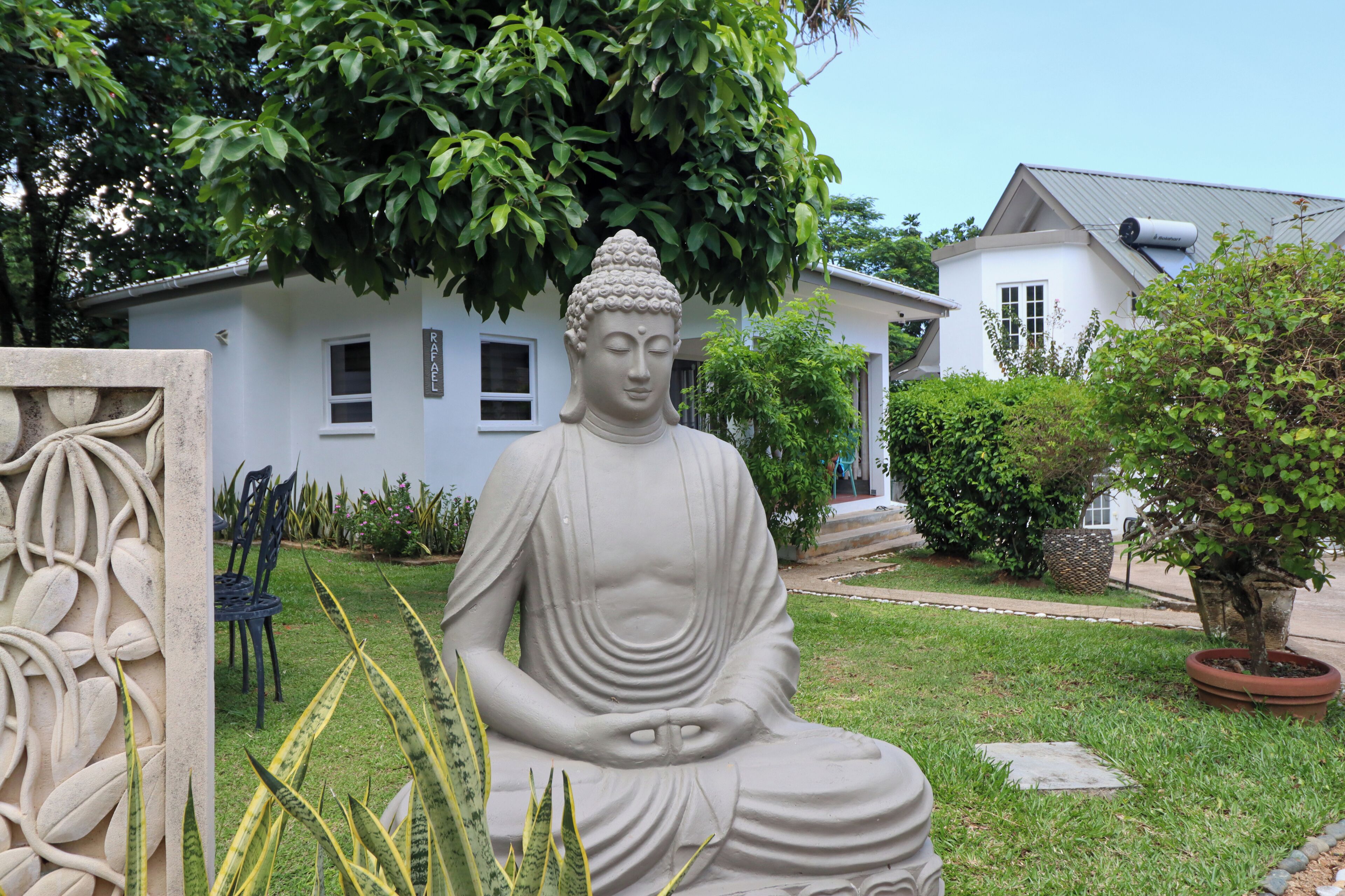 Une statue de Bouddha dans un jardin, avec un bâtiment blanc en arrière-plan.