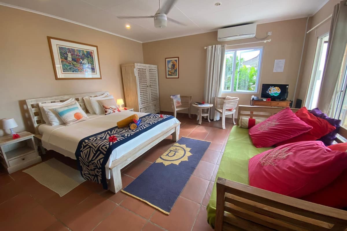 Habitación de hotel con cama, escritorio con televisor, silla, ventilador de techo y ventana con cortinas.