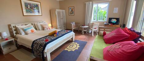 A hotel room with a bed, a desk with a TV, a chair, a ceiling fan, and a window with curtains.