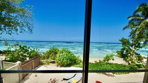 A view of a beach from a balcony with a wooden railing, a red kayak, and lounge chairs.
