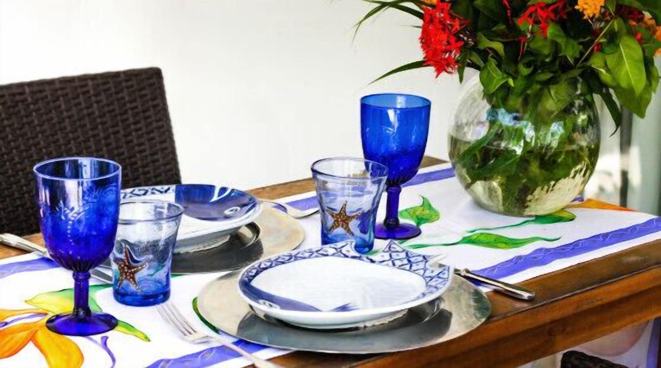 Una mesa puesta con cristalería azul, un plato blanco y un cuenco de plata.