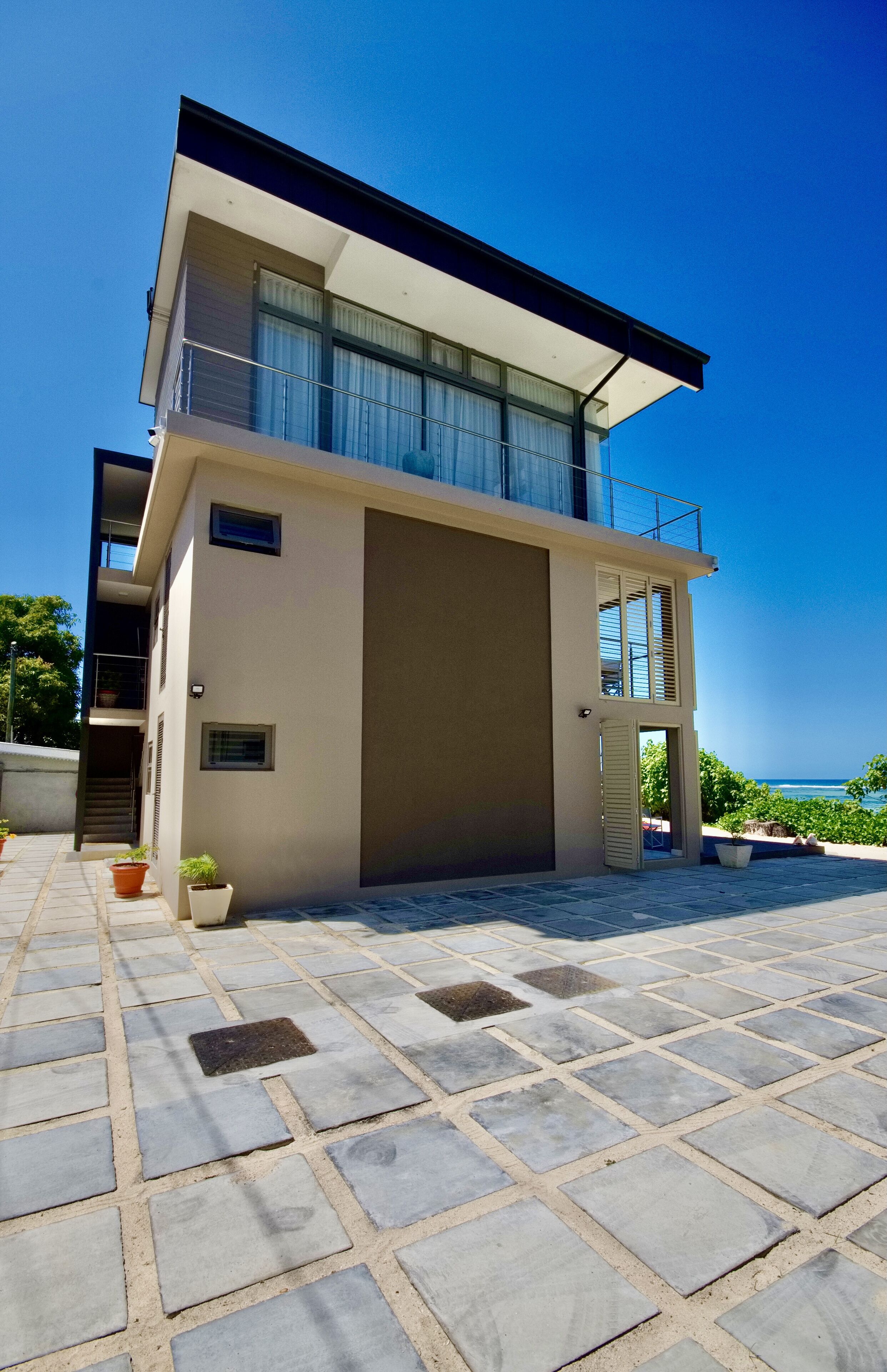 A modern two-story building with a balcony, a large garage door, and a paved patio area.