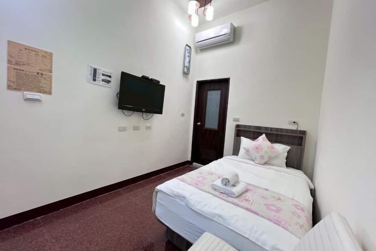 A hotel room with a bed, a television, an air conditioning unit, and a door.