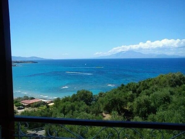 A coastal view with a clear sky, a mountain in the distance, and lush greenery in the foreground. - Sofos Apartments (Zakynthos)