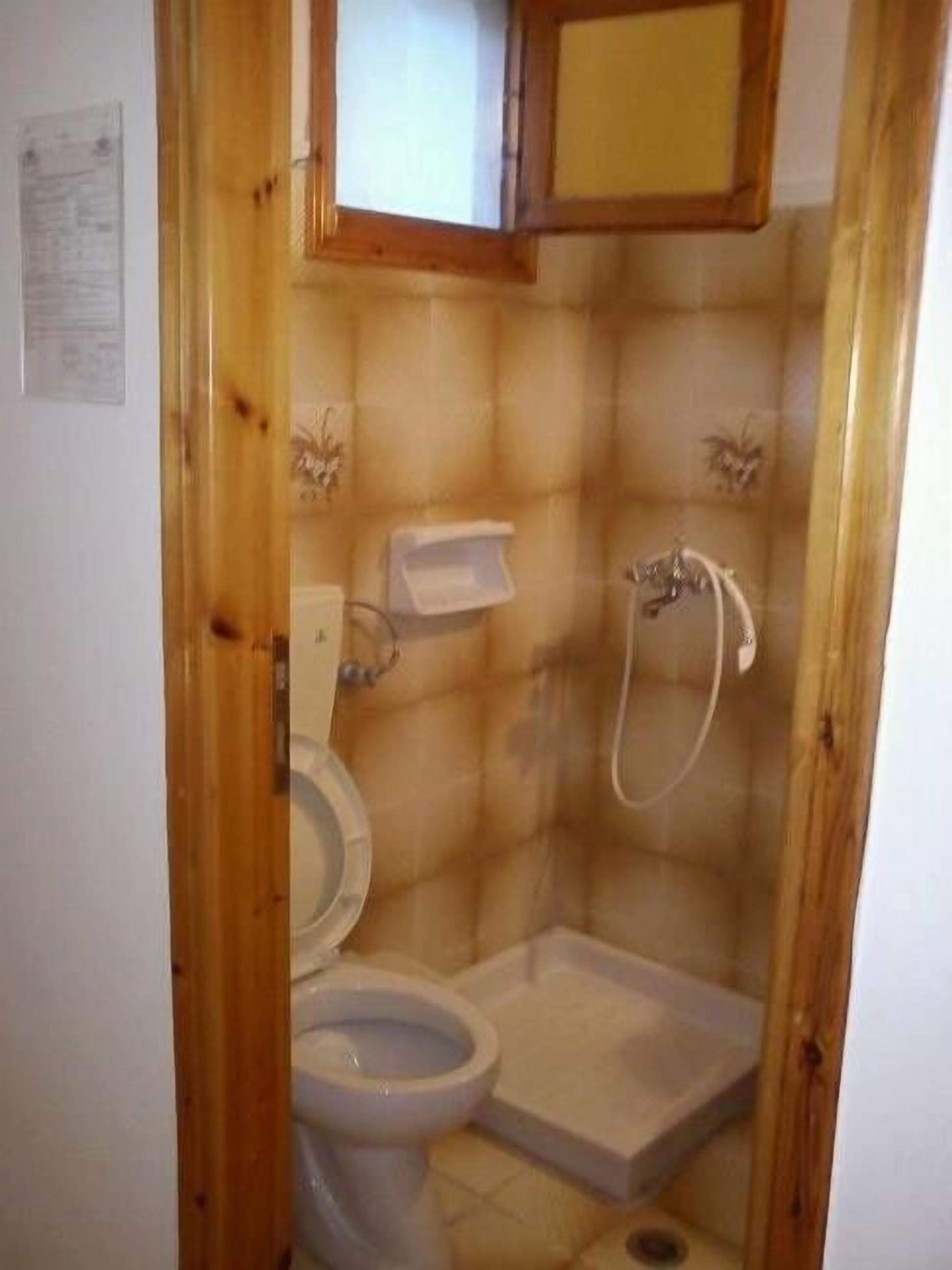 Un baño pequeño y cerrado con inodoro, ducha y puerta de madera.