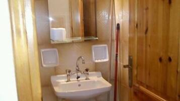 Ein kleines Badezimmer mit Waschbecken, Spiegel und Holztür.