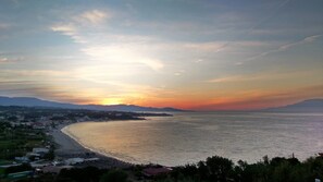A coastal landscape with a beach, a town in the background, and mountains in the distance.