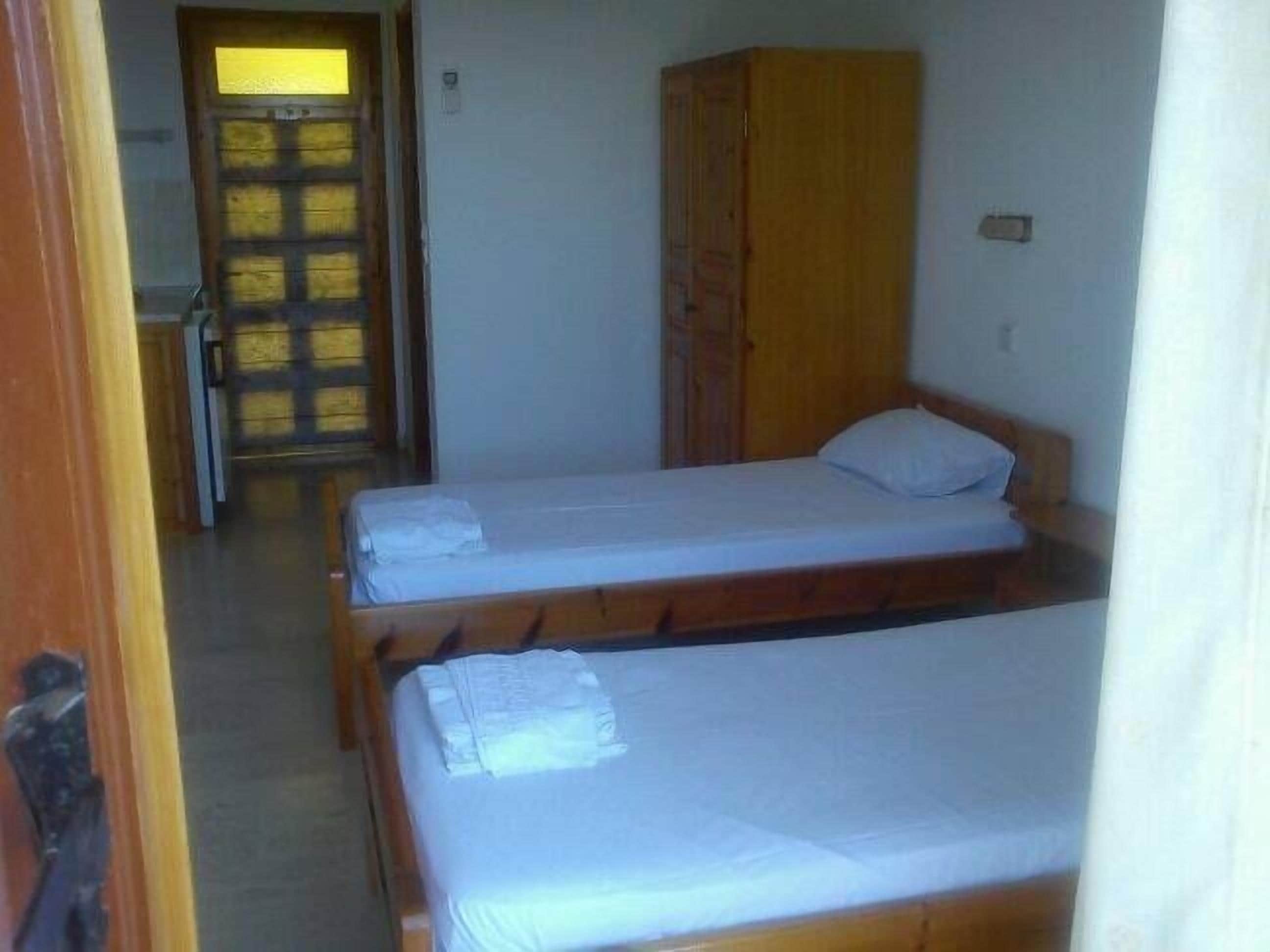 A room with two single beds, a wooden wardrobe, and a door leading to another room.