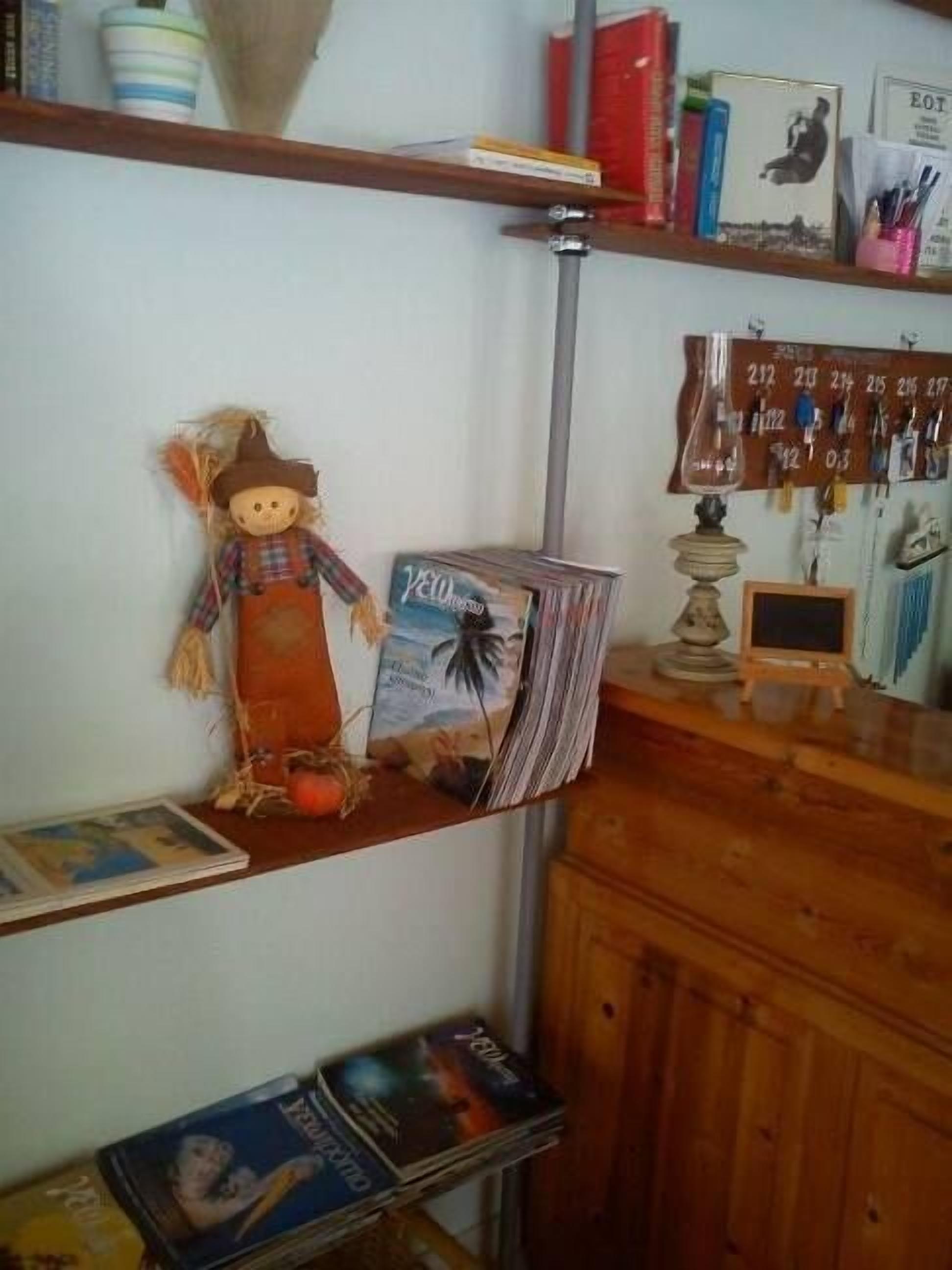 A shelf with a decorative scarecrow, a stack of magazines, and a small TV on a wooden cabinet.