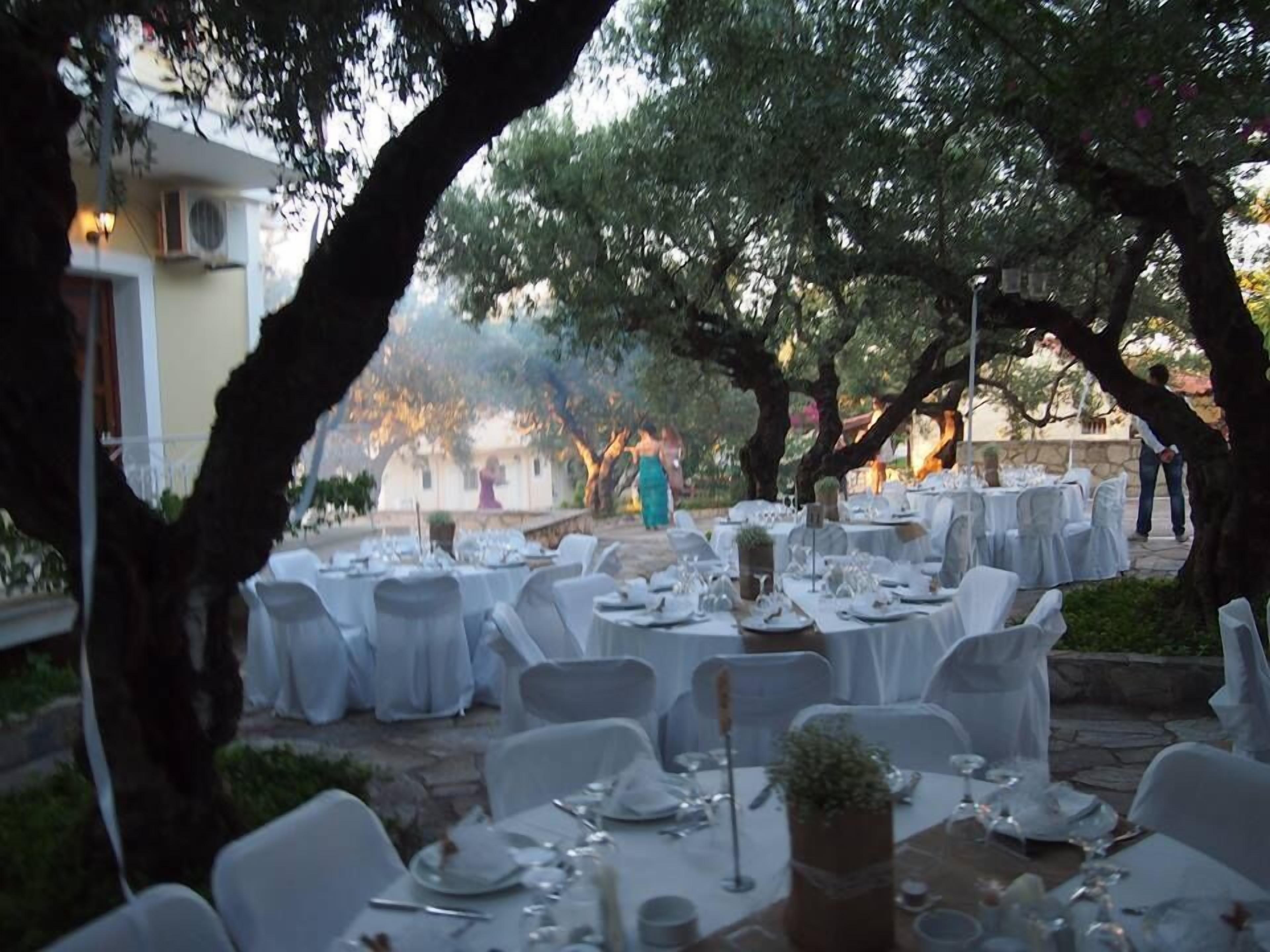 An outdoor dining area with round tables set for a meal, surrounded by trees.