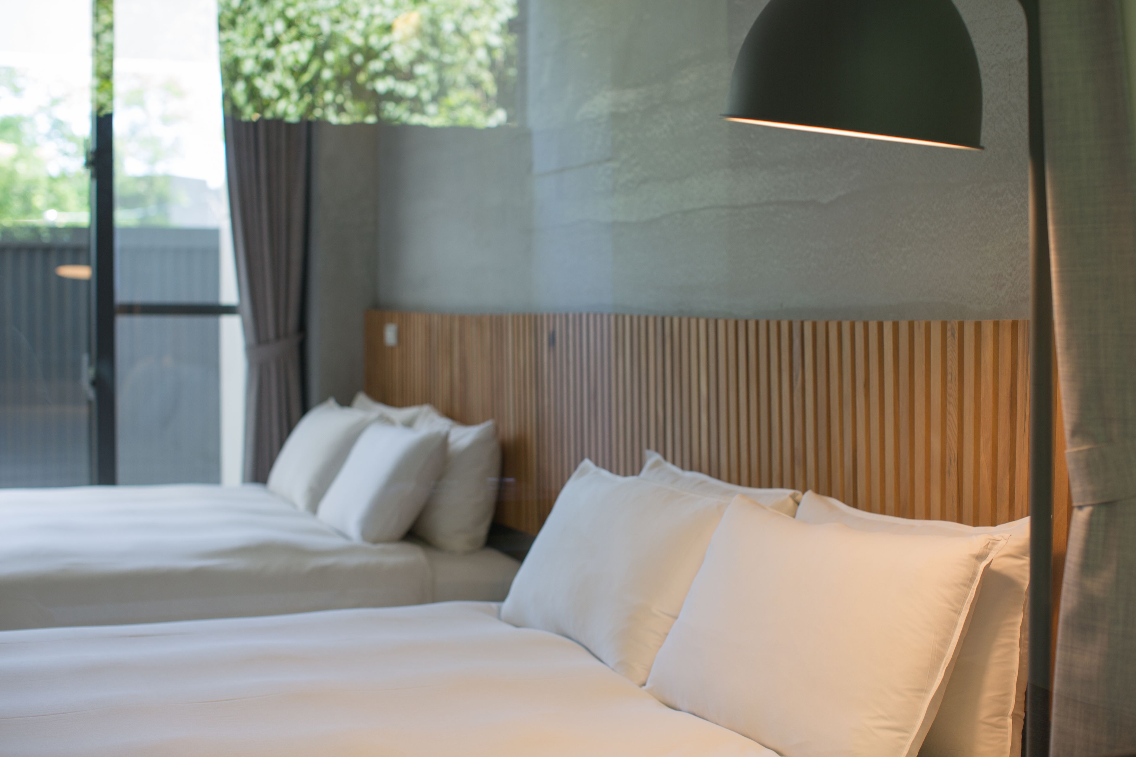 Una habitación de hotel con dos camas, un cabecero de madera y un amplio ventanal con cortinas.