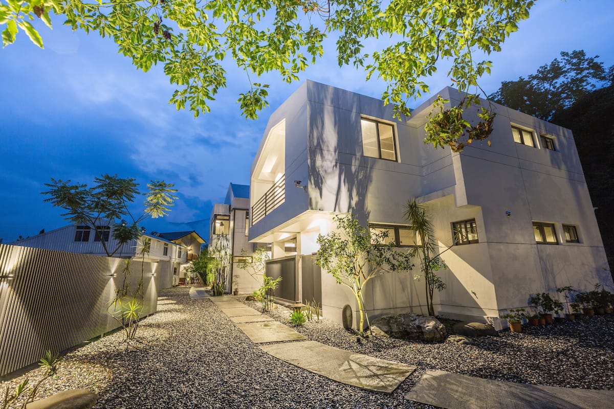 Uma casa moderna de dois andares com acesso por um caminho de cascalho e cerca de madeira.