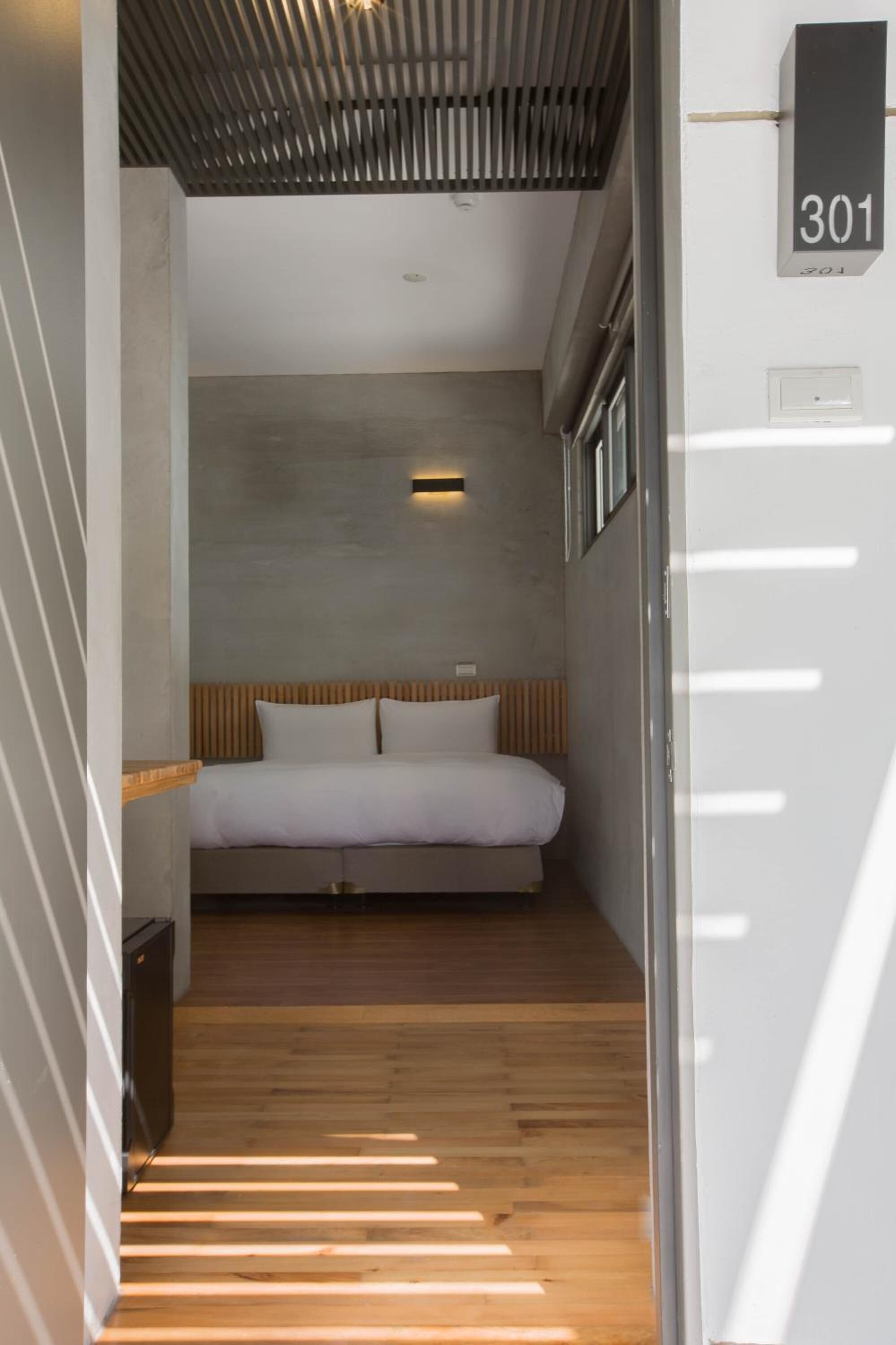 A modern hotel room with a bed, wooden flooring, a slatted ceiling, and a number sign indicating room 301.
