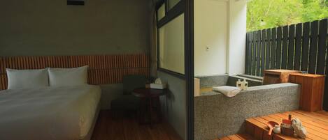 A modern hotel room with a bed, a small table, a seating area with a view, and a balcony with a wooden deck.