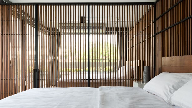 Une chambre moderne avec un grand lit, des lattes en bois et une vue sur l’extérieur.