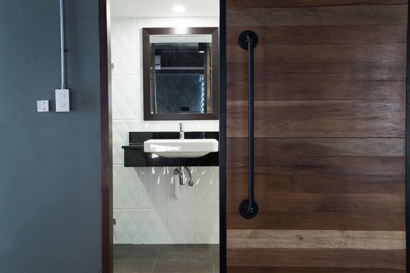 A bathroom with a wooden door, a white sink, and a mirror above it. - Nord Studio (Chiang Mai)