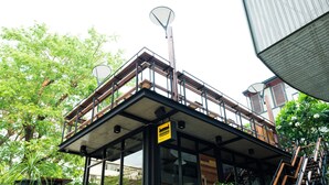Un bâtiment moderne avec une façade en verre, un espace extérieur aménagé pour les clients et une enseigne indiquant qu’il s’agit d’un restaurant.