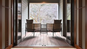 Un interior moderno con suelo de madera, dos sillones de mimbre, una mesita y un ventanal con vistas a árboles.