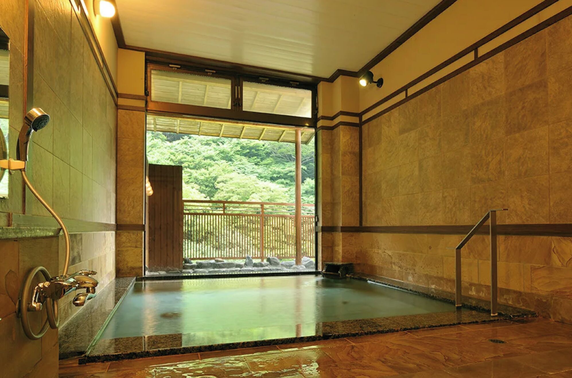 A traditional Japanese onsen with a wooden interior, a view of a forested area through the sliding door, and a stone floor.