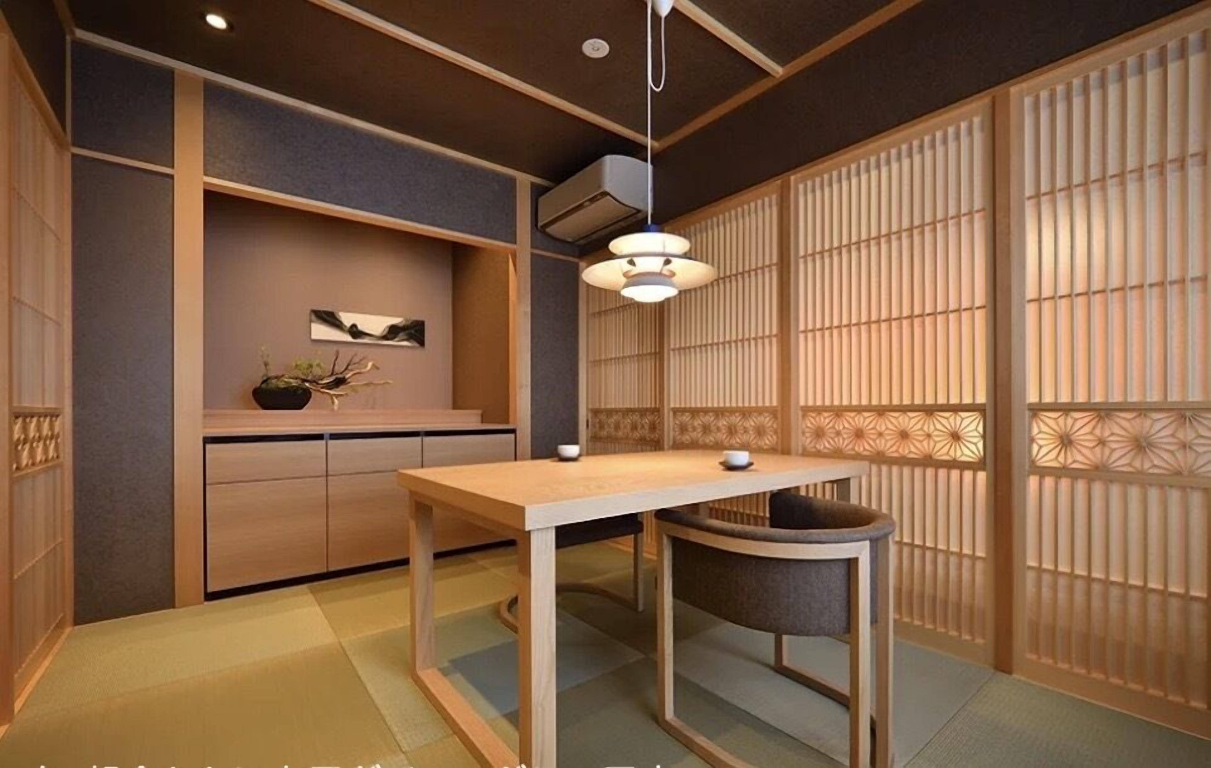 A traditional Japanese room with tatami flooring, a low table, a chair, a hanging light fixture, and a sliding shoji screen.