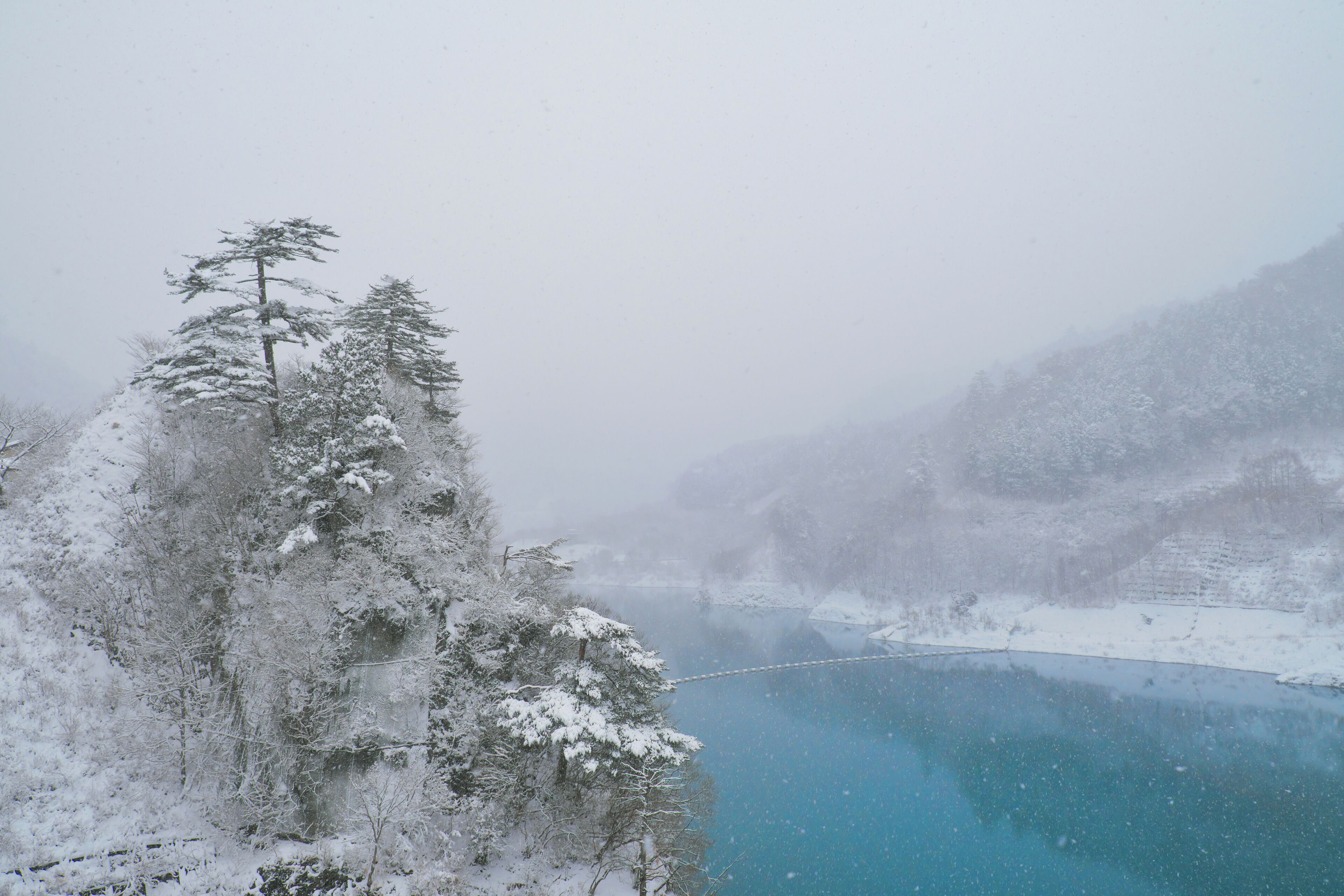 Un paisaje montañoso nevado con un lago azul cristalino y un puente colgante.