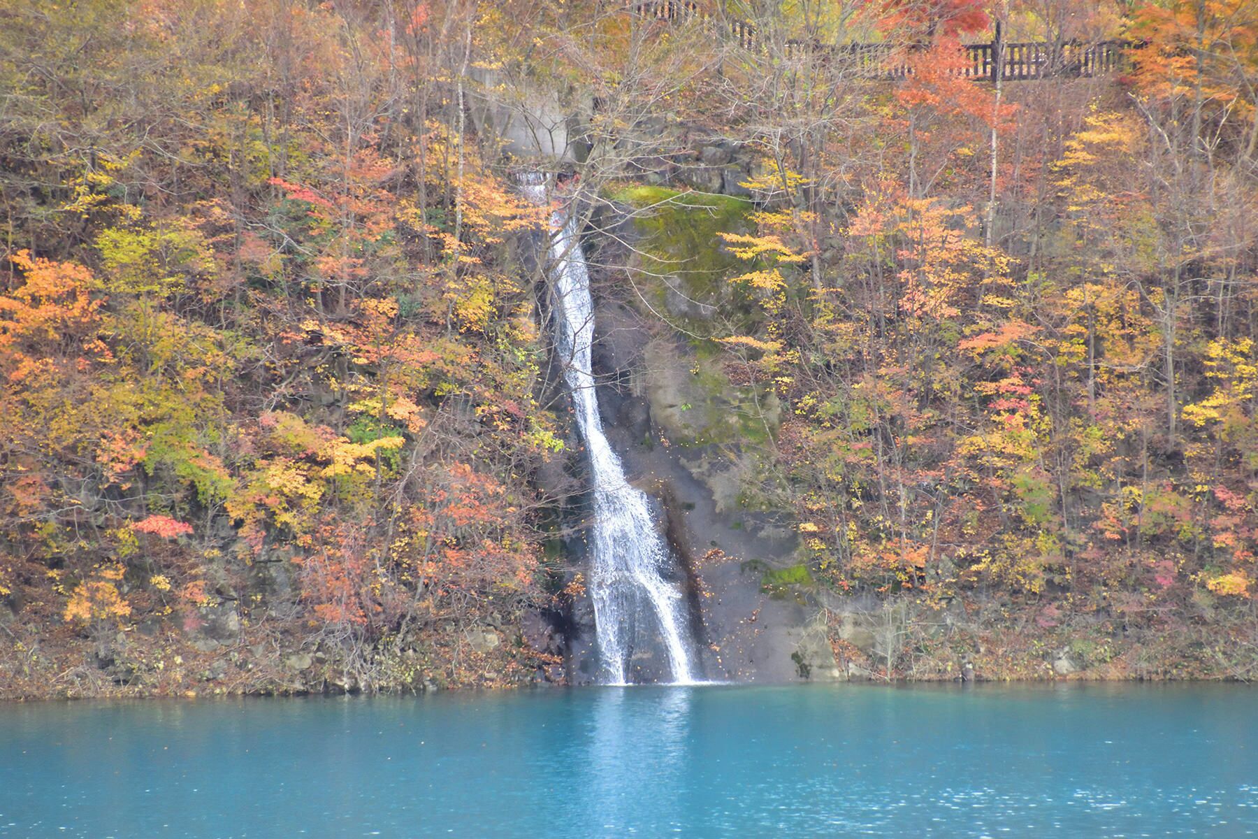 Una cascada que desemboca en un lago rodeado de árboles de colores otoñales.