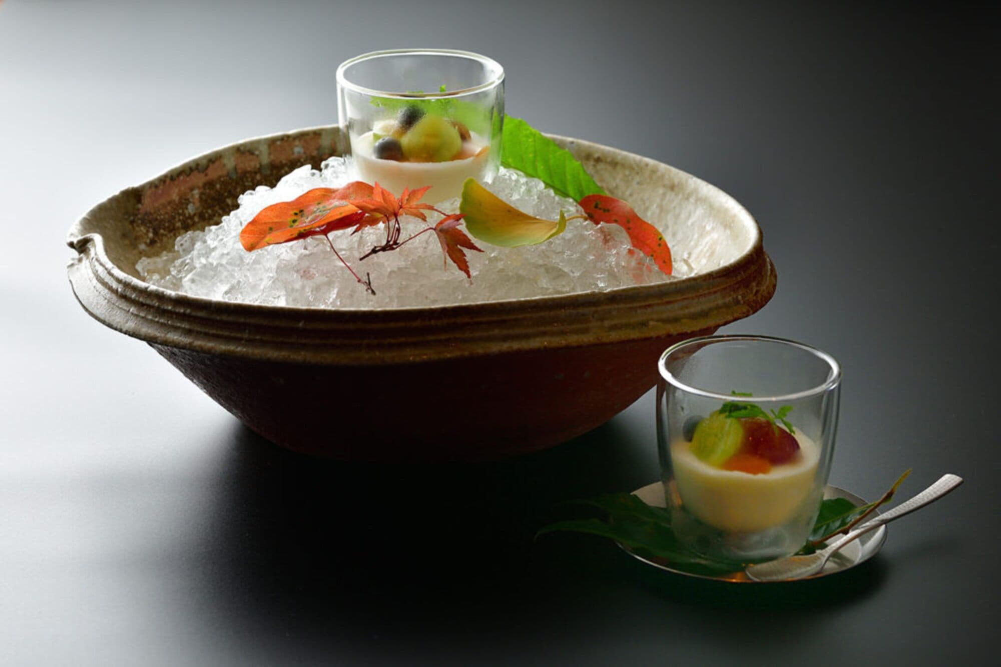 A bowl of ice with three glasses of a layered dessert, garnished with leaves and berries.