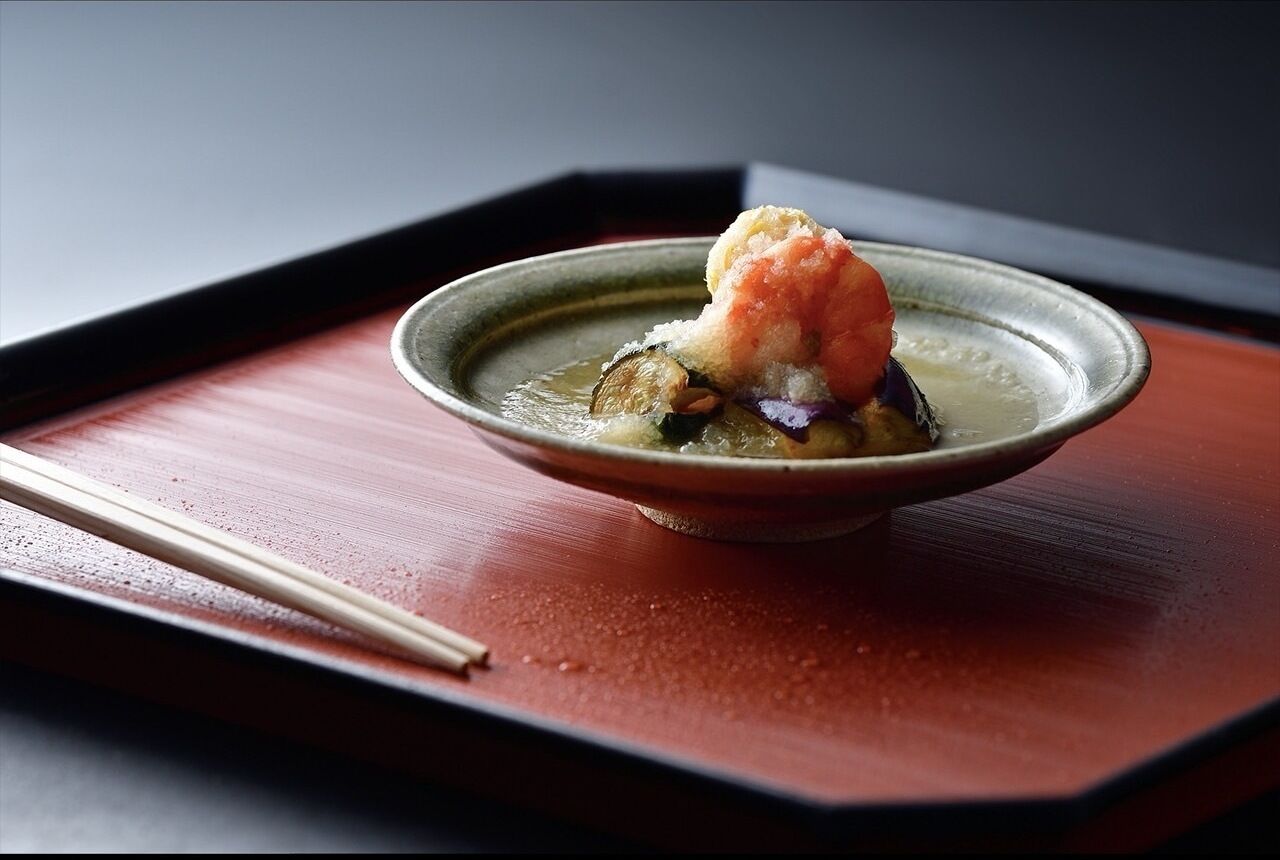 A bowl of soup with a piece of fish and a dumpling on a wooden tray.